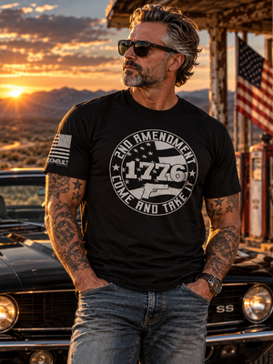 Man wearing FreedomBuilt 2nd Amendment 1776 Come and Take It graphic tee in Black Heather, printed with soft water-based ink, standing beside a classic black Camaro at sunset.